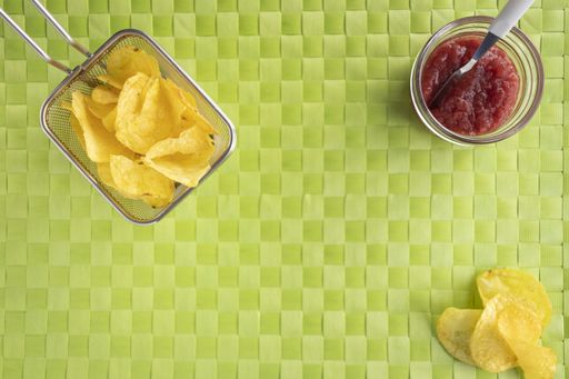 A high angle shot of a basket of potato chips and a bowl of jam on a woven green surface