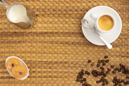 A high angle shot of a cup of coffee, milk, donuts, and coffee beans on a woven surface