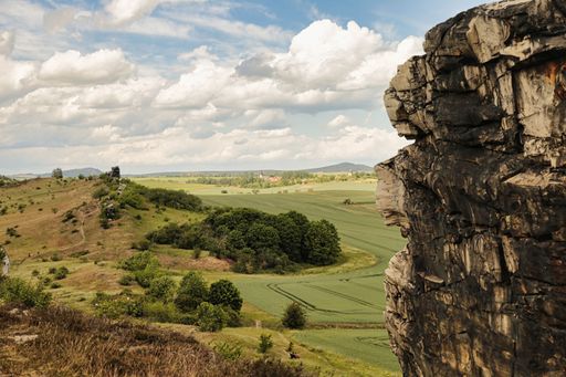 A beautiful landscape of forested hills under a cloudy sky with a rocky cliff in the foreground
