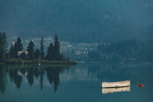 A small boat reflected on the calm Green Lake surrounded by dense forests and buildings