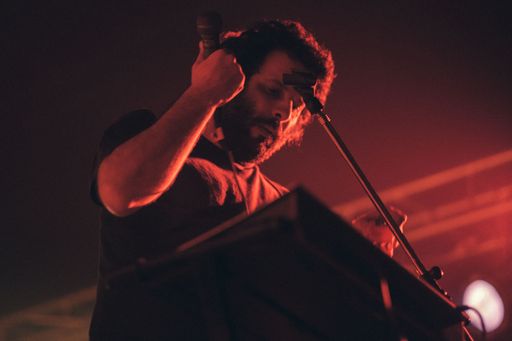 A Caucasian male singer performing on the stage against a background of red lights