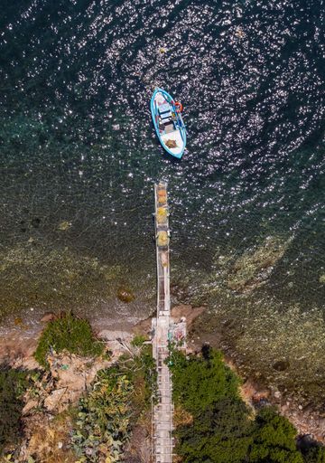 A topdown aerial view of a fishing boat moored near a small dock