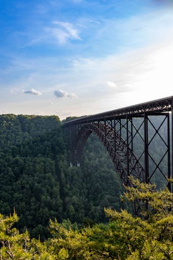 A vertical shot of New River Gorge Bridge under the beautiful sky with green forest in the background