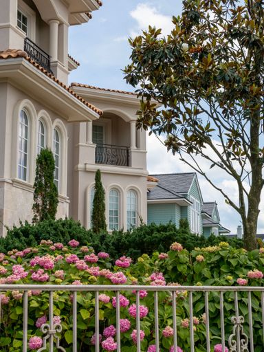 A vertical shot of a beautiful white building with flowers and a fence in front