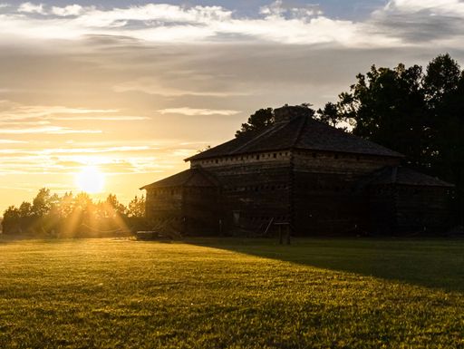 A scenic view of bright sunset over a field and a house in the countryside