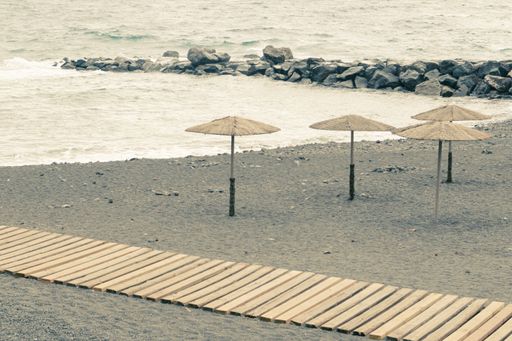 A beautiful shot of straw umbrellas and a wooden path on a rocky beach