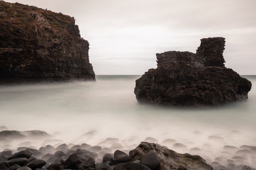 A beautiful long exposure shot of white water flow surrounding large rock formations in a sea