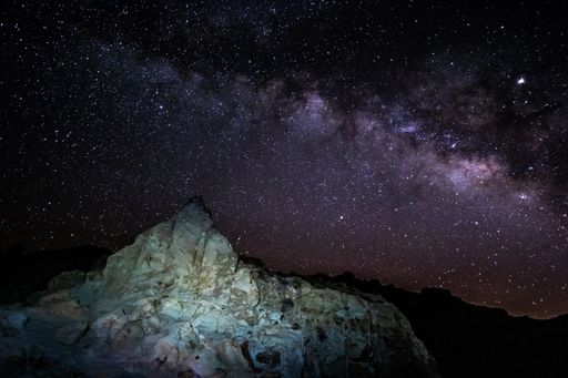A beautiful shot of a large rock formation under a purple starry galaxy sky
