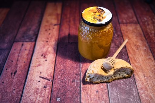 A closeup of a honey jar and bread in a wooden surface