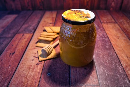 A closeup of a honey jar and cookies on a wooden surface