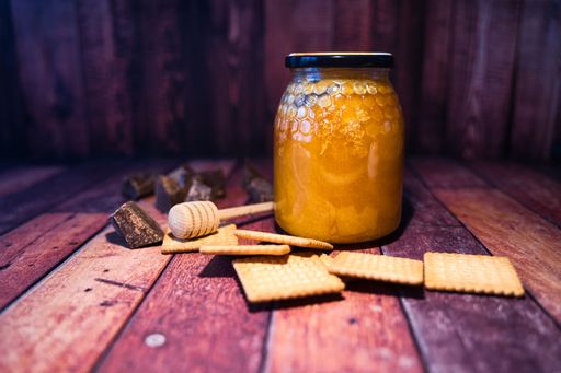 A closeup of a honey jar and cookies on a wooden surface