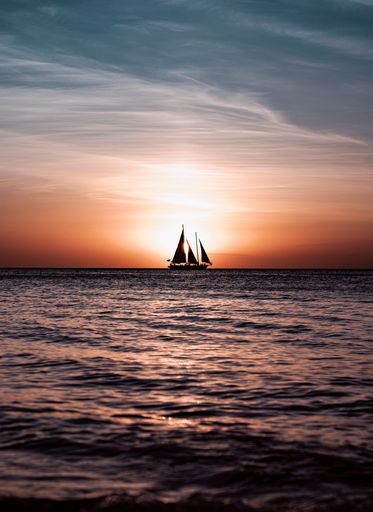 A silhouette of a three-masted sailing ship on sea with calm waves during the sunset