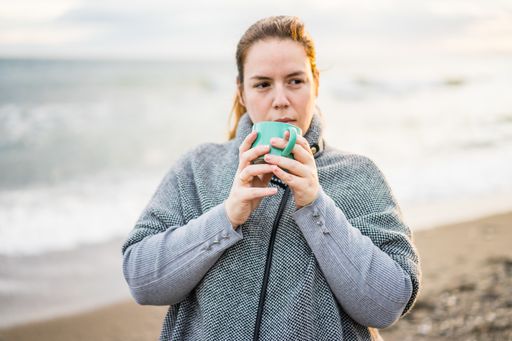 A closeup shot of a caucasian female drinking coffee from a small mug outdoors