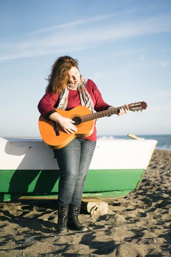 A vertical shot of a caucasian female standing and playing a guitar on a beach