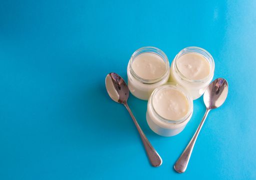 Three yogurts in glass jars and two teaspoons on a blue background
