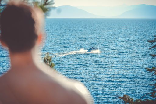 A horizontal shot of a person looking at the motorboat near the sea surrounded by beautiful mountains