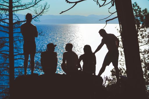 A horizontal silhouette shot of five people near the beautiful sea with the reflection of bright sun rays