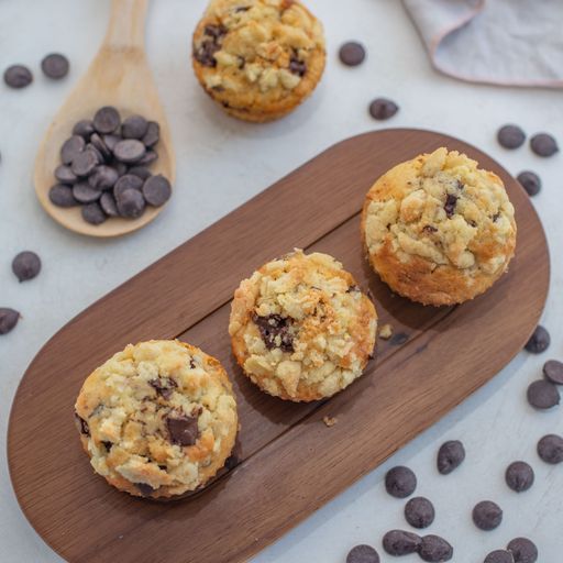 A closeup of sweet homemade muffins with streusel, cream, and chocolate chips on a wooden board