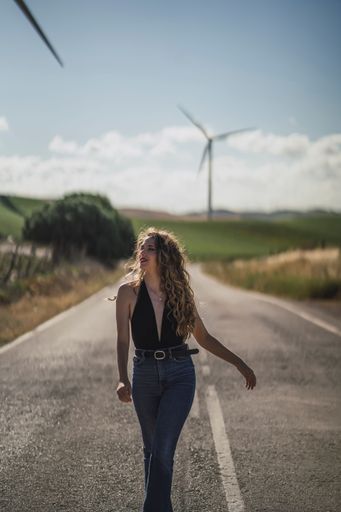 A vertical shot of a beautiful Caucasian female walking on a road near a field with wind turbines
