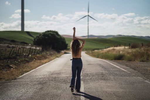 A back view of a young Caucasian female on a road with a blur background of a field with wind turbines