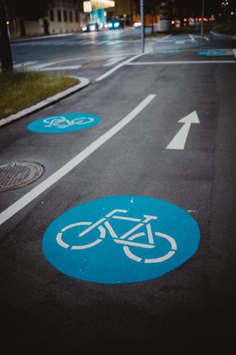 A vertical shot of a bike lane with a blue circle, a white bicycle sign and an arrow during the night