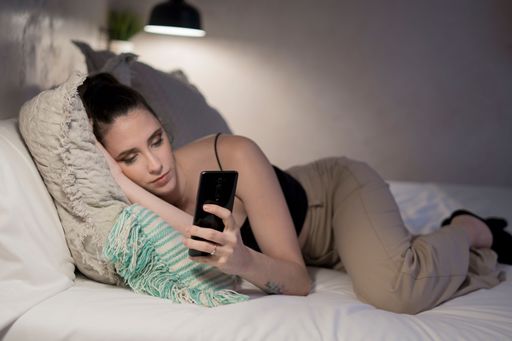 A young woman using her smartphone while lying on bed