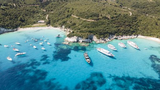 A drone shot of a beautiful seacoast with yachts moored along the shore and blue water
