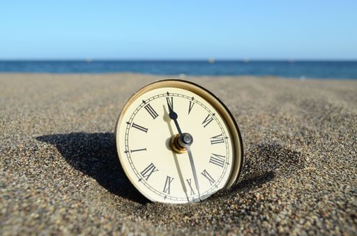The close-up view of an alarm clock with roman numbers on the sand before the seascape