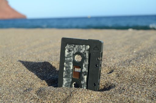 The close-up view of a music cassette halfway in the sand before the seascape