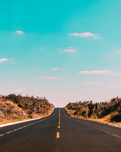 A vertical shot of empty road under blue sky and white clouds