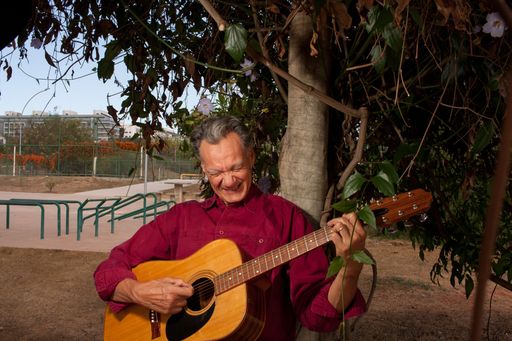 Happy Mature Man singing and playing his acoustic guitar in the park