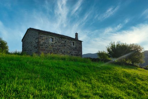 A small stone cottage on the hill in lush green countryside under blue cloudy sky in Cantabria, Spain
