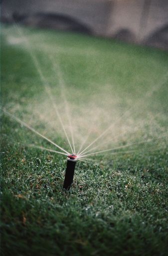 A vertical shot of an automatic lawn sprinkler watering green grass in a blurred background
