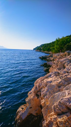 A vertical shot of a beautiful blue sea washing the rocky shore
