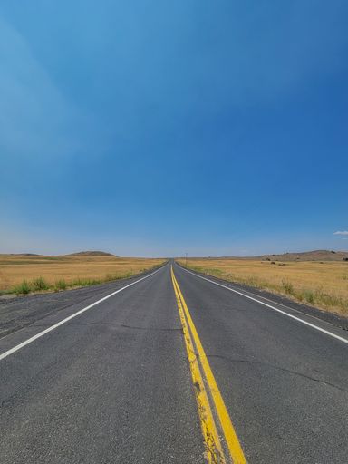 A long empty asphalt highway through open fields in Washington state on blue sky background