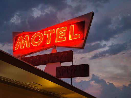 A low angle shot of red neon motel sign against dark cloudy sky background