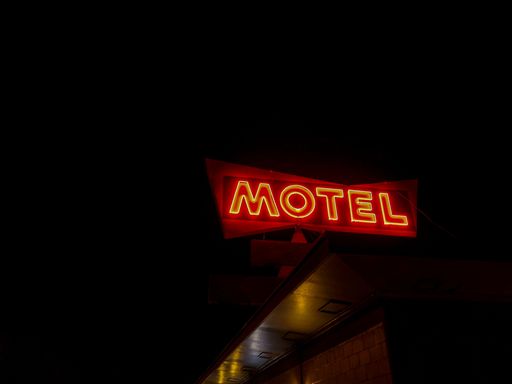 A low angle shot of red neon motel sign against black sky background