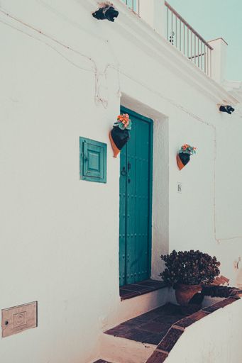 A vertical shot of a white house with a bright blue door decorated in Frigiliana, Spain