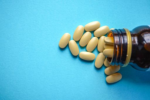 A closeup shot of painkiller pills spilling out of a dark blue vial isolated on a cyan background