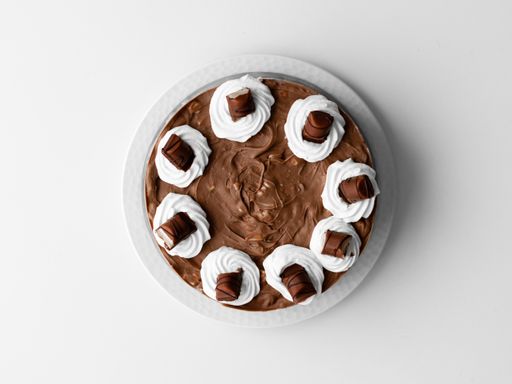 A top view of a chocolate cream cake with whipped cream and chocolate pieces on a white surface