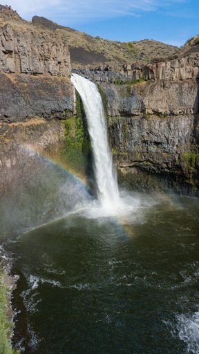 A vertical shot of the Palouse Falls with the rainbow over it in the United States