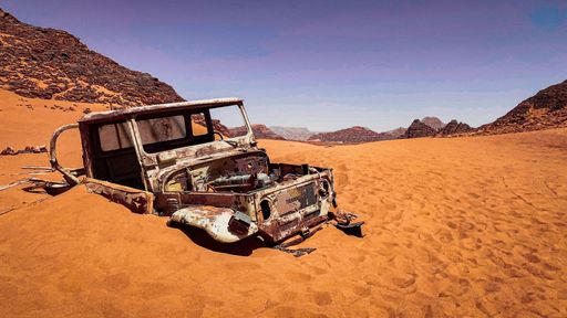 An abandoned old car at a dessert with rocky hills in the background