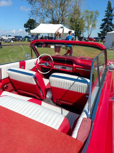 Red and white interior of old Chevrolet Chevy Impala SS Super Sport V8 convertible 1964 in the countryside. Nature grass and trees. Classic car show