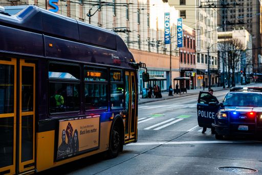 A trolleybus heads down 3rd Avenue in Seattle, passing by a Police car, with police officers standing neraby