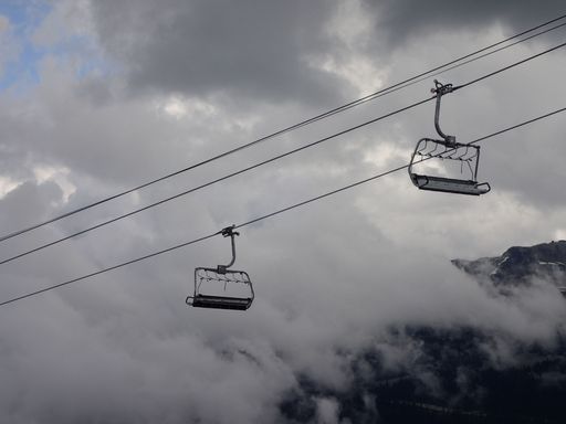 Two chairlifts hanging on a rope outlined against a cloudy sky