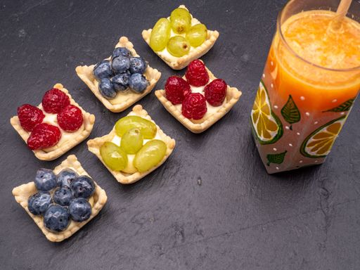 A high angle shot of small delicious fruit cup pastries and a glass of orange juice