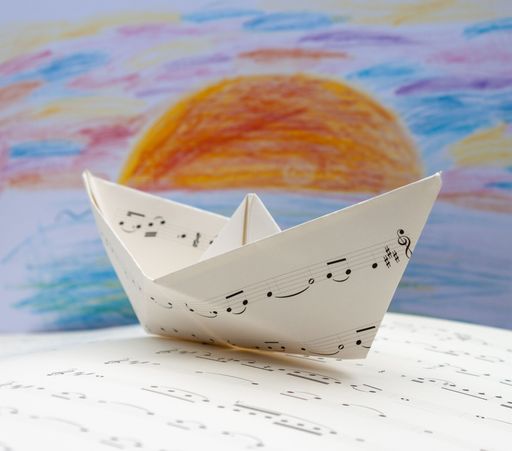 A paper boat made out of music sheet on the background of a child's drawing of sun