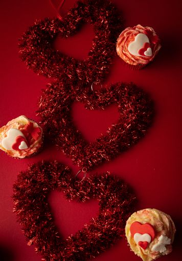 a vertical high angle shot of valentines day themed red cupcakes with hearts and a heart ornaments