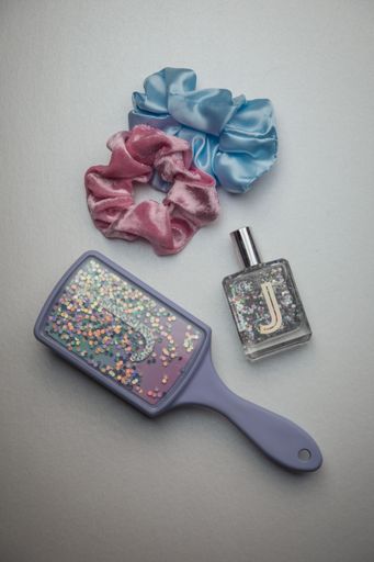 A vertical shot of a hair brush, perfume and scrunchies
