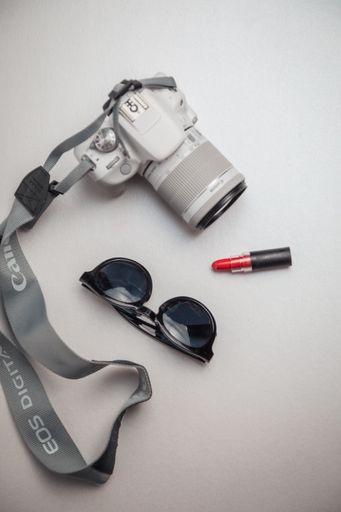 A vertical shot of a limited white canon camera with lipstick and sunglasses
